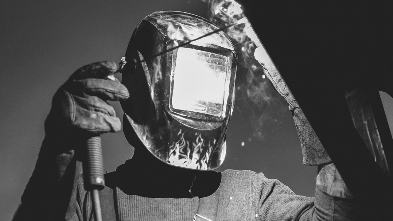 Un soldador protegido con un casco para soldar sostiene una pinza para electrodos revestidos de Duroxite