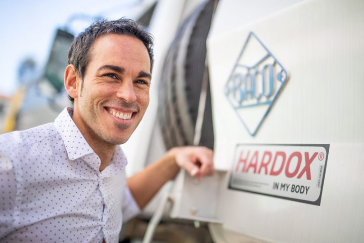 A smiling operations manager from Industrias Baco next to a truck with a Hardox® In My Body sign of quality.
