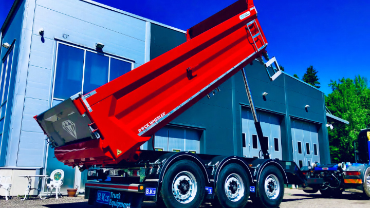B.K:s의 시설 외부에서 Hardox® 500 Tuf 제품으로 제작된 적재함이 있는 밝은 빨간색 덤프 트럭 트레일러에서 하역하고 있습니다.