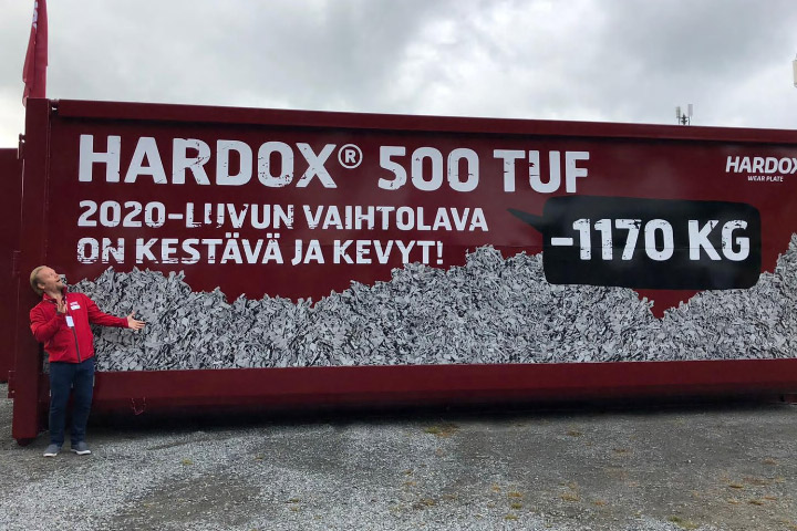 Un container en acier rouge vif fabriqué en acier Hardox 500 Tuf, portant une inscription en finlandais, dans la forêt. 
