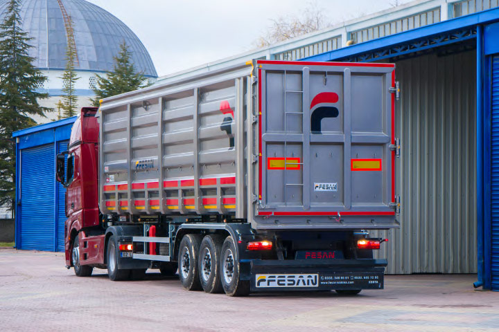 A silver and red dumper trailer made by Fesan coming out of a warehouse.