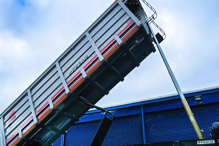A dump trailer body made in Hardox® 500 Tuf, lifted high against a blue sky.