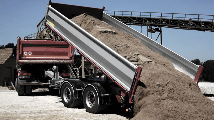 An open-bed tipper body dumping out a heavy load of dirt and rocks.