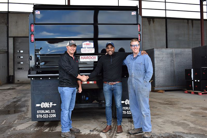 Three smiling men in front of the first Colt-branded dump truck made of Hardox® 500 Tuf, from Industrial Welding Supply. 