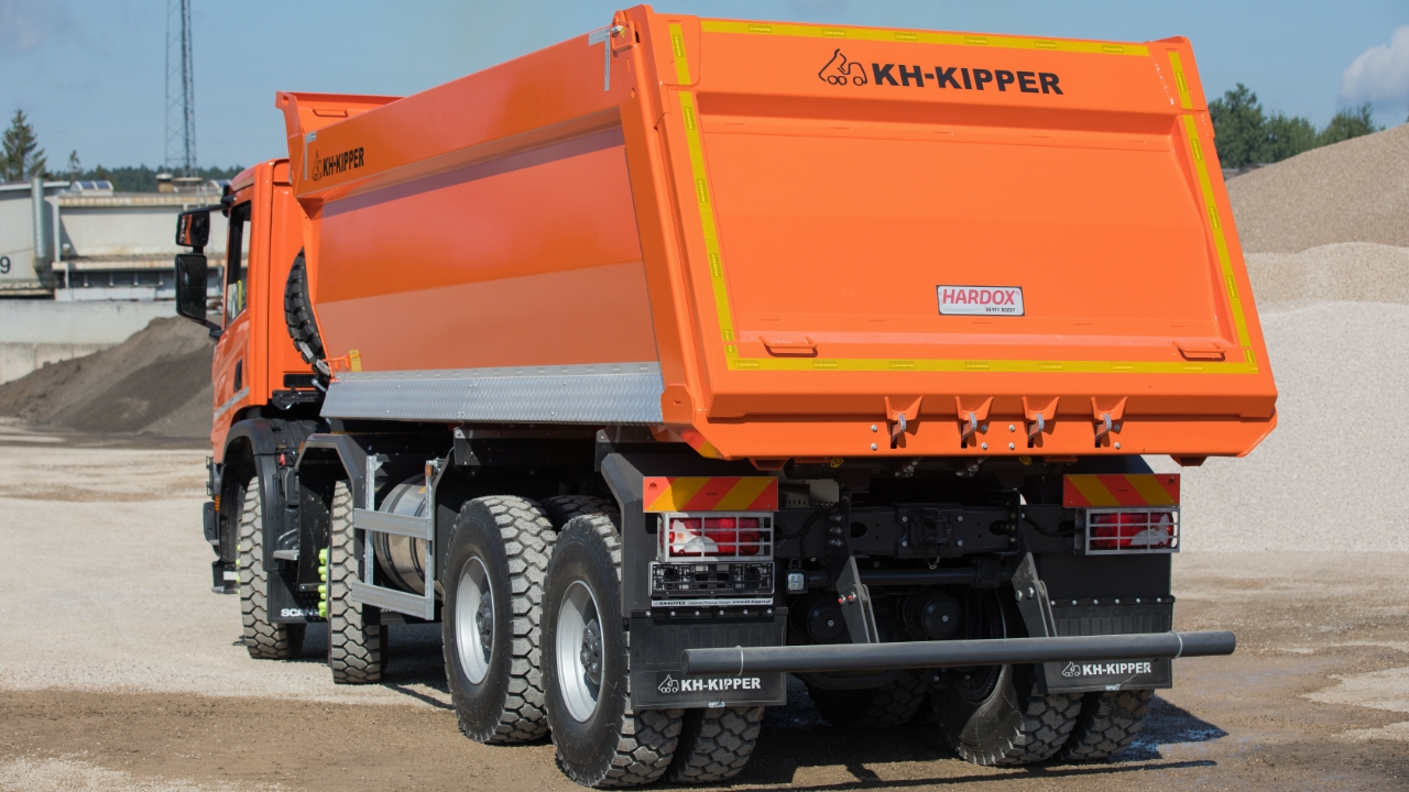 A KH-Kipper truck with an orange body photographed from behind 