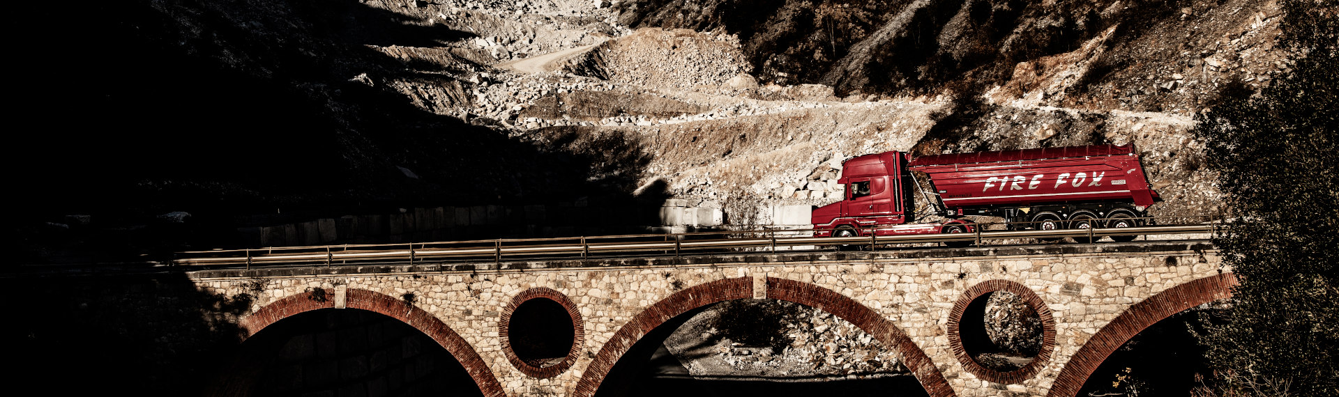 Hardox 500 Tuf çelik plakadan yapılmış parlak kırmızı bir Fire Fox kamyon köprüden geçiyor