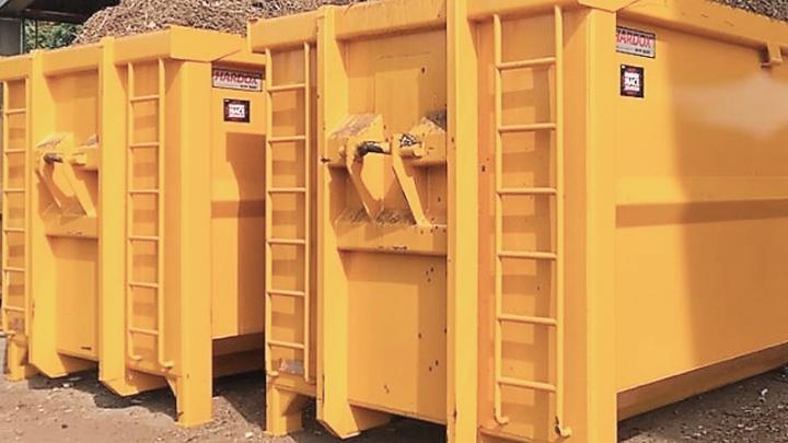 Dva žluté otevřené kontejnery se značkou kvality Hardox® In My Body, naložené korozivní dřevní štěpkou.