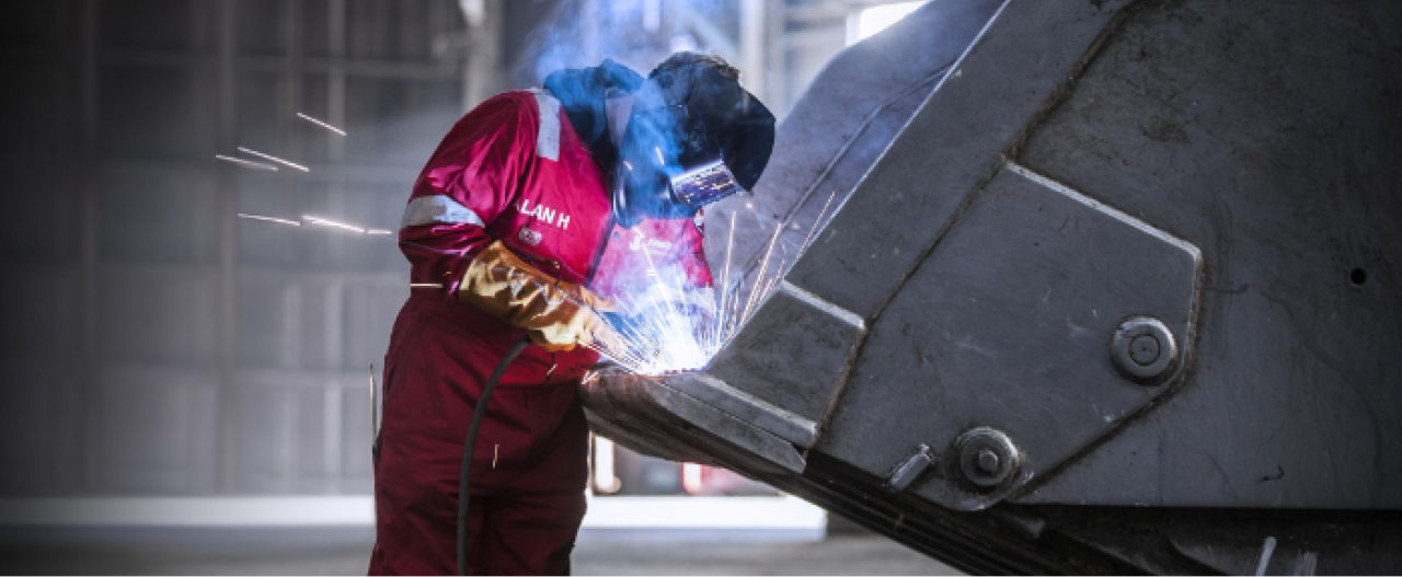 A welder with hard hat, welding an AR steel plate made in high-strength Hardox 400 wear plate, inside an excavator bucket.
