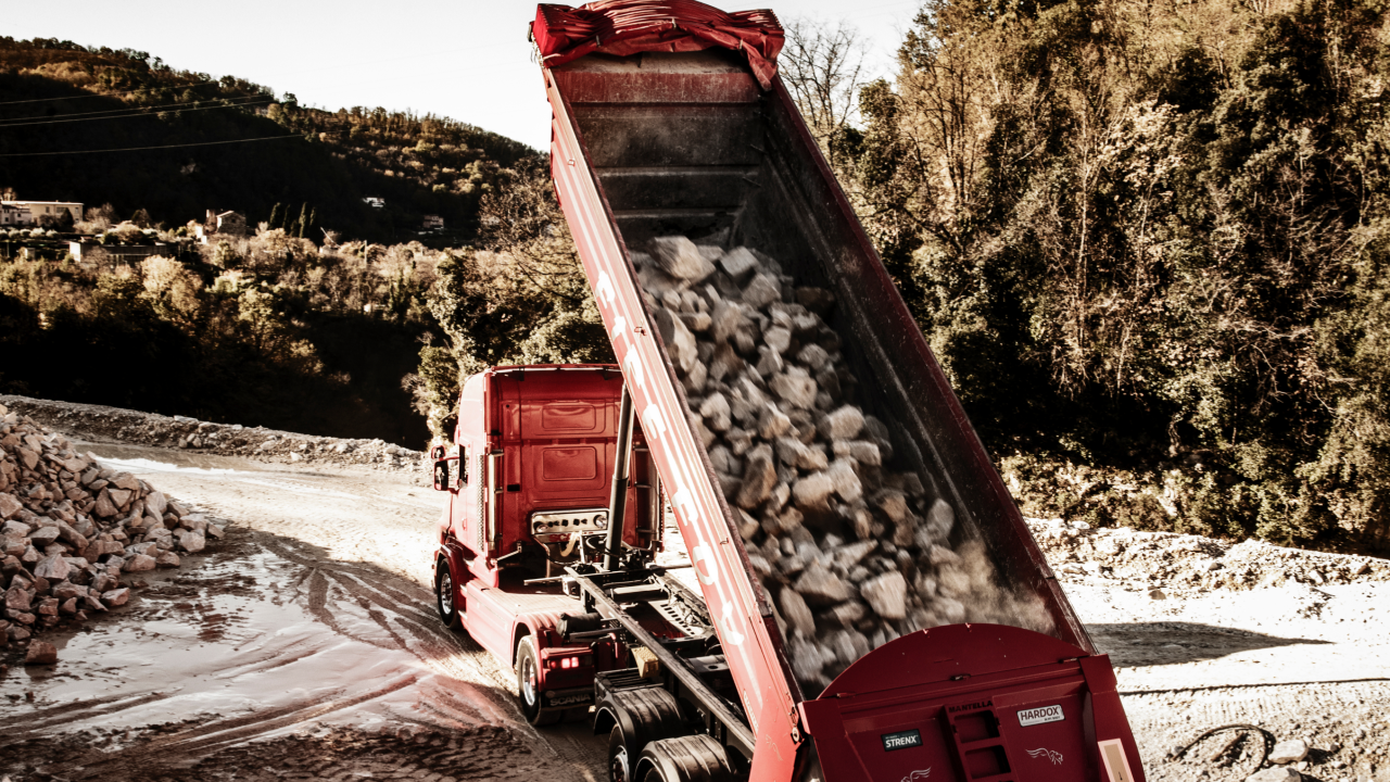 Red dump body made in Hardox® 500 Tuf steel dumping out some abrasive rocks.