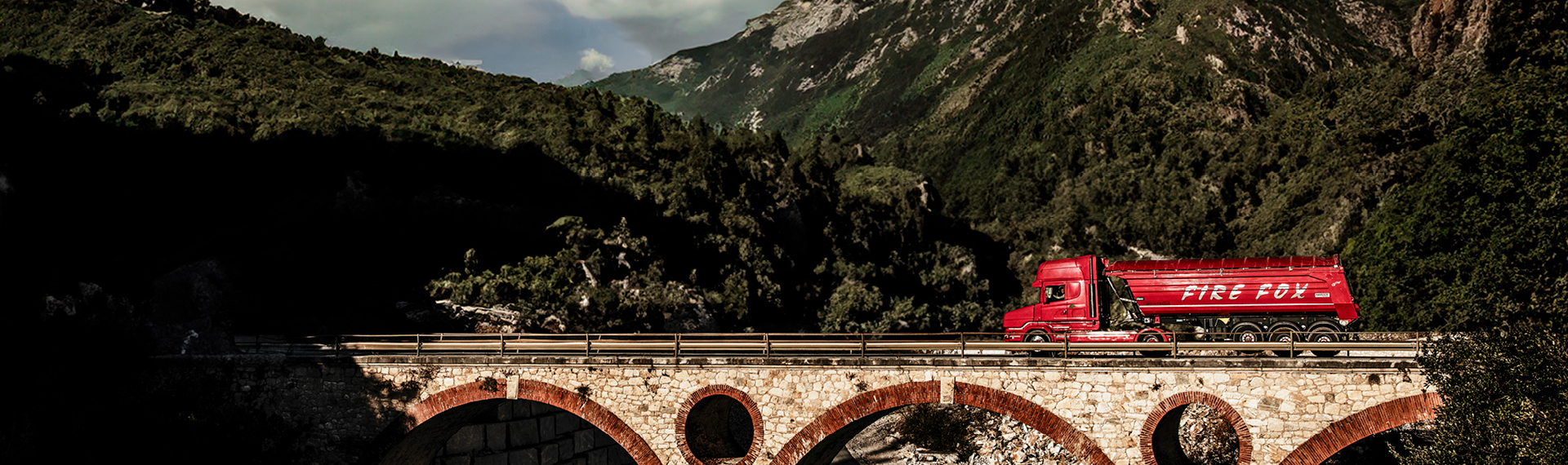 Red truck with body made in Hardox® steel in a lightweight design, driving across a stone bridge.