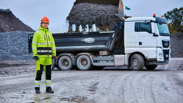 A mine worker in front of a heavy-duty truck with truck body made in Hardox® wear plate.