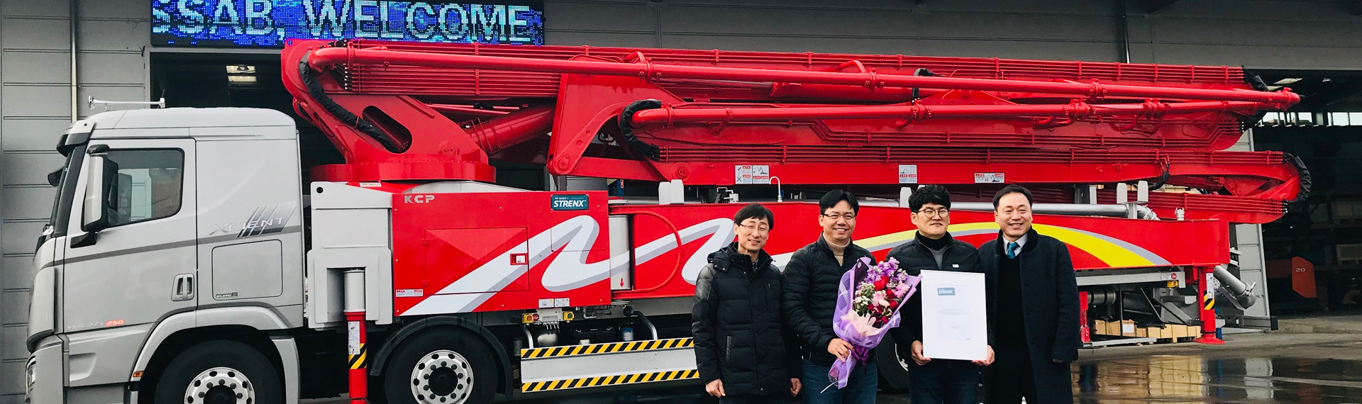 Camión de bombeo de hormigón de color rojo brillante con empleados de KCP orgullosos de poseer un certificado de My Inner Strenx